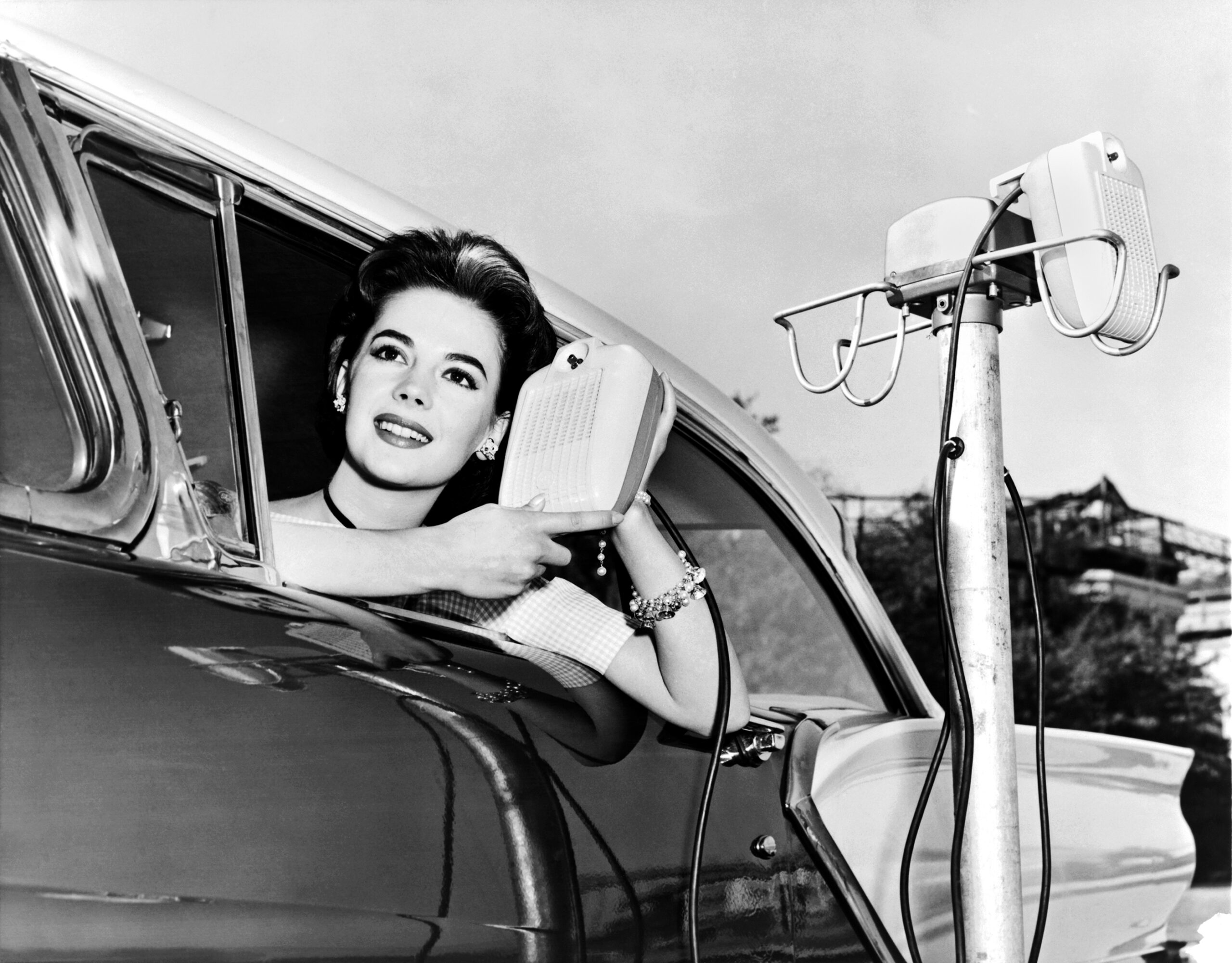 Natalie Wood displays the new drive in-movie speakers as she leans out of her car window, Hollywood, California, 1957