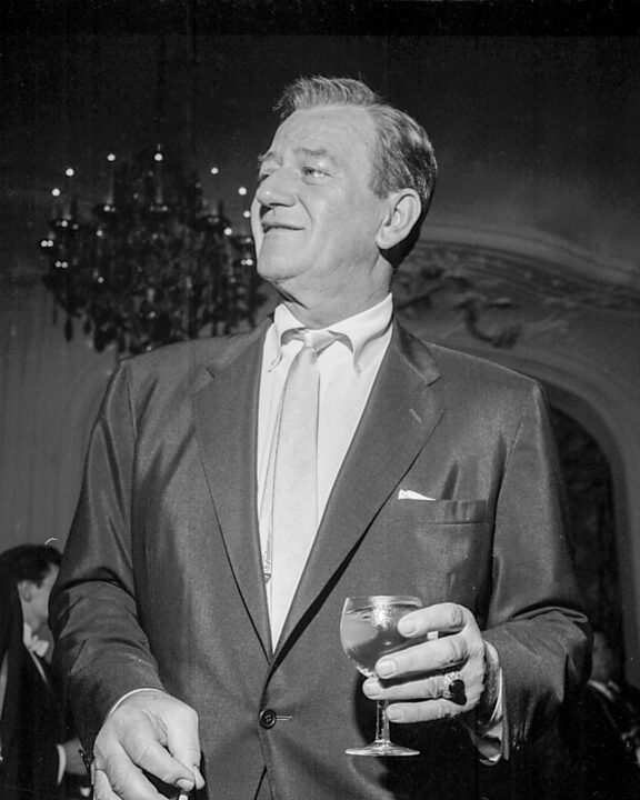 American actor John Wayne (1907 - 1979) holding a glass of wine at an event, circa 1965.