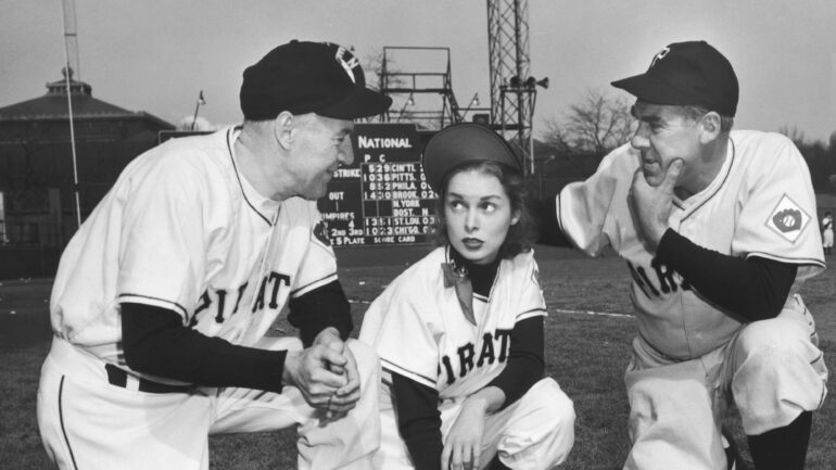 Paul Douglas and Janet Leigh in a scene from the 1951 baseball fantasy film Angels in the Outfield. They are both crouched down on a baseball field, wearing Pirates uniforms.