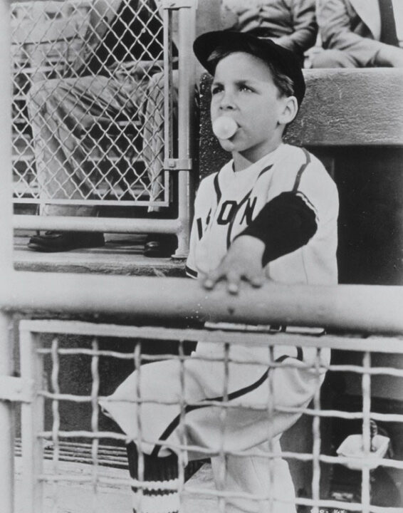 A scene from the 1953 black-and-white baseball comedy film <i>The Kid From Left Field</i>. Picture depicts a 10-year-old boy (played by Billy Chapin) leaning up against a railing in a baseball dugout and blowing a bubble with bubblegum after being named manager of a fictional baseball team.