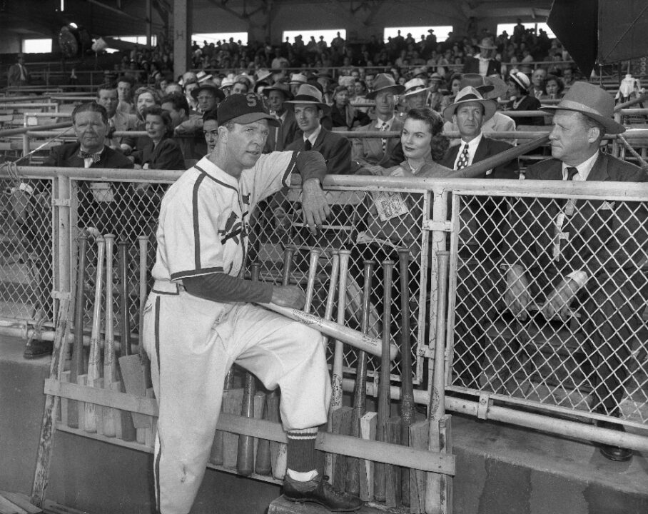 A scene from the 1952 sports biopic <i>The Pride of St. Louis</i>. Dan Dailey as legendary baseball pitcher Jerome "Dizzy" Dean, wearing a St. Louis Cardinals uniform and leaning up against a railing in a baseball stadium. Seated on the other side of the railing is Joanne Dru, who plays Dean's wife, Patricia Dean.