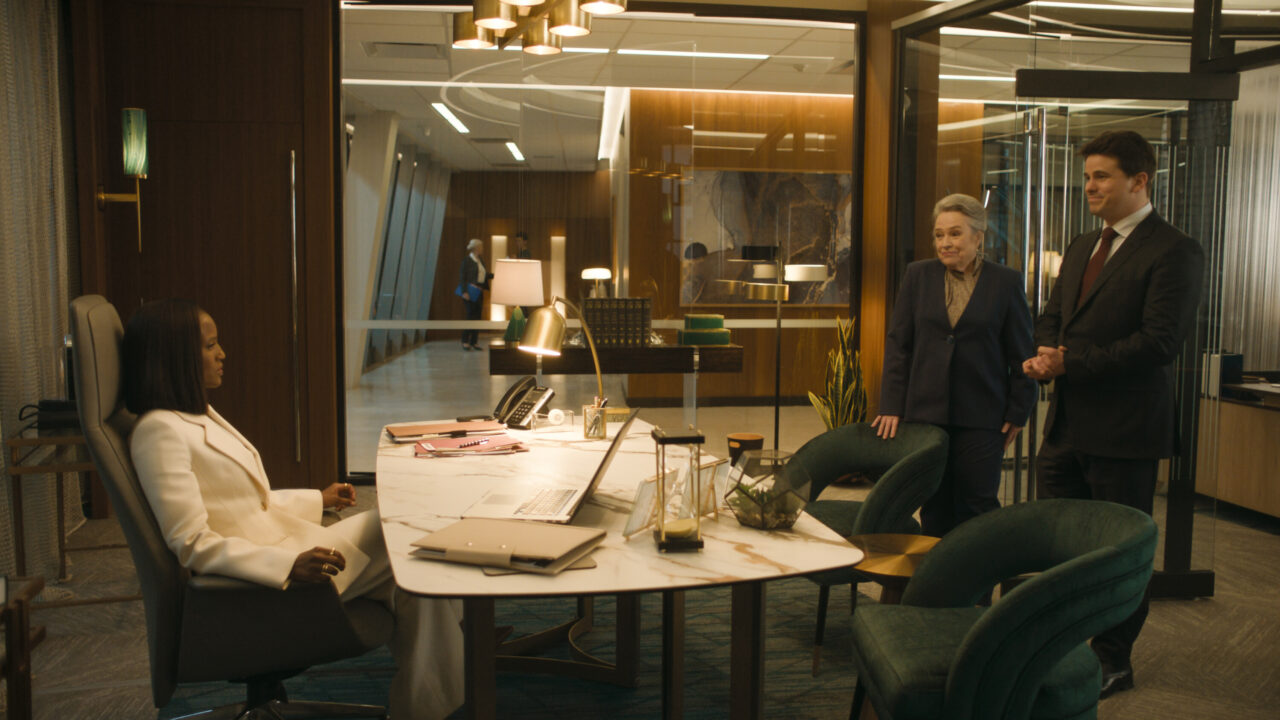 A shot from CBS' upcoming legal drama series <i>Matlock</i>, which is inspired by the 1986-95 Andy Griffith-led series of the same name. The shot is in a large office at a law firm. On the far left of the photo, seated behind a desk, is Skye P. Marshall as senior attorney Olympia Lawrence. She is a Black woman wearing a white business suit, and she is looking across the desk at two people standing to the far right side of the photo. The leftmost one of these two people (as seen by one looking at the photo) is Kathy Bates as Madeline "Matty" Matlock, wearing a dark business jacket over a beige dress shirt. To her immediate right is Jason Ritter as Julian Monroe, another lawyer at the firm. He is wearing a dark business suit, white dress shirt and maroon business tie.