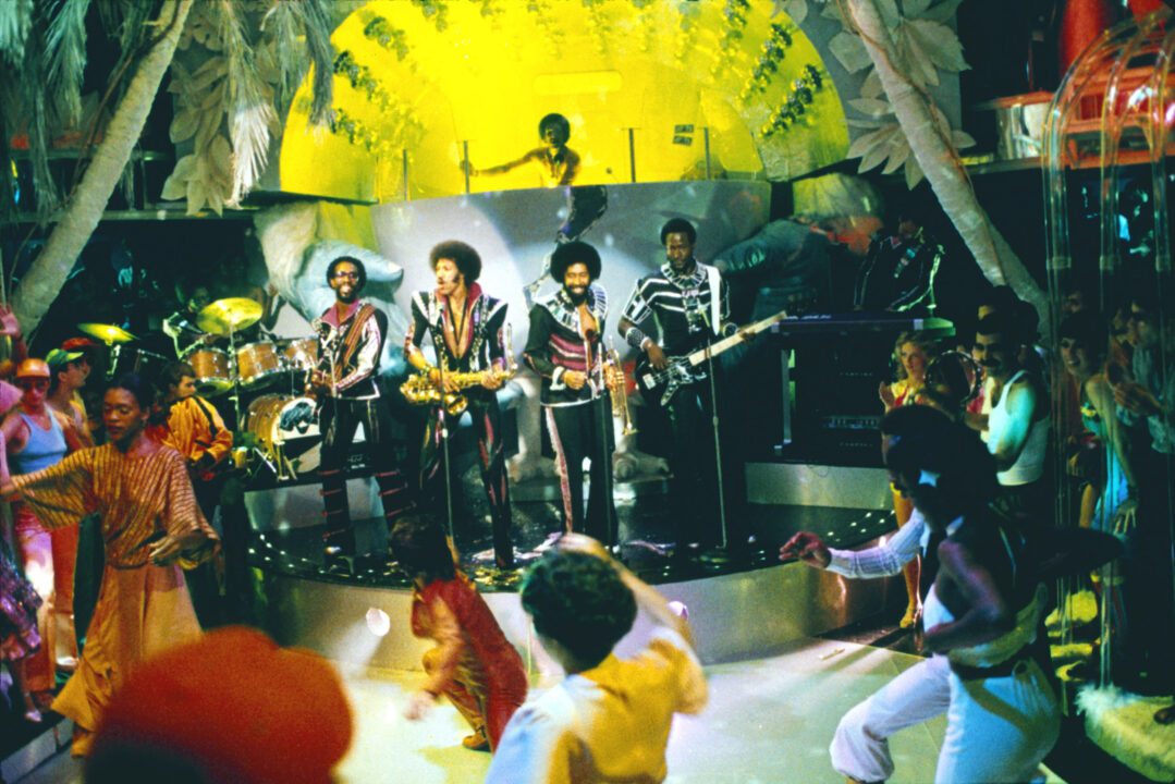 shot of The Commodores performing as themselves at a disco club in the 1978 movie "Thank God It's Friday." They are on a stage as dancers groove on the dance floor below.