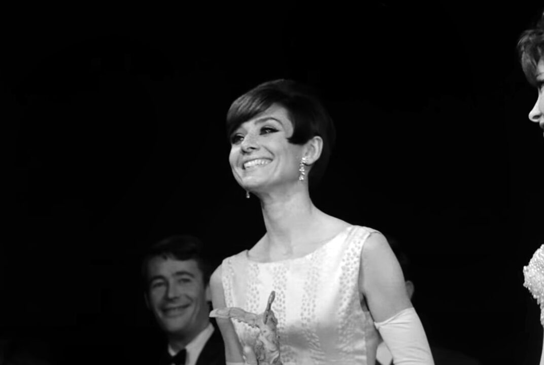 AUDREY: MORE THAN AN ICON, from left: Peter O'Toole looking on as Audrey Hepburn receives a 1964 Victoire du cinema francais award from Gina Lollobrigida, October 1965, Paris, 2020