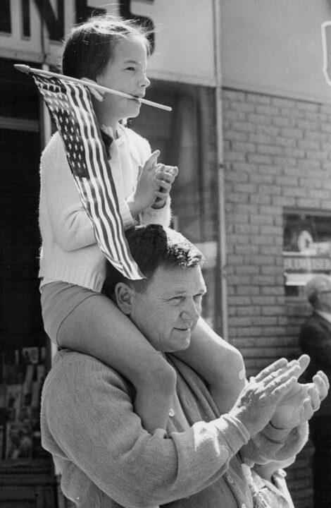 MAY 30 1970, MAY 31 1970 Missy Morehead, 8, of 458 Gilpin St., used her teeth to hold her flag when she had to use her hands to clap during Memorial Day parade Saturday. Missy is perched on shoulders of her father, R.W. Morehead