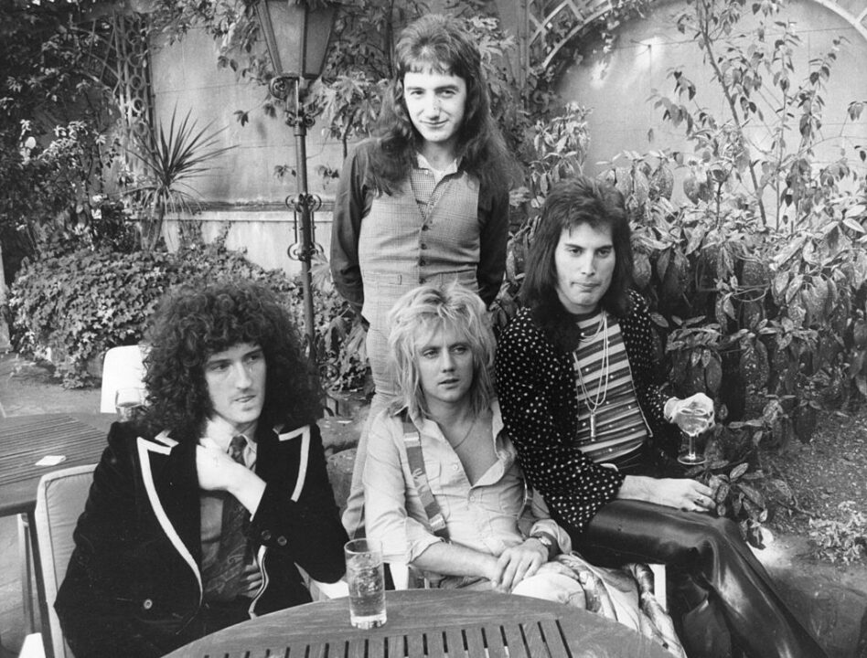 September 1976: British rock group Queen at Les Ambassadeurs, where they were presented with silver, gold and platinum discs for sales in excess of one million of their hit single 'Bohemian Rhapsody', which was No 1 for 9 weeks. The band are, from left to right; Brian May, John Deacon (standing), Roger Taylor and Freddie Mercury (Frederick Bulsara, 1946 - 1991).