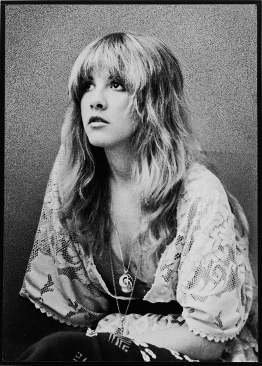 Promotional portrait of American pop and rock singer Stevie Nicks (of the group Fleetwood Mac) as she sits and looks upward, dressed in a lace shawl, late 1970s