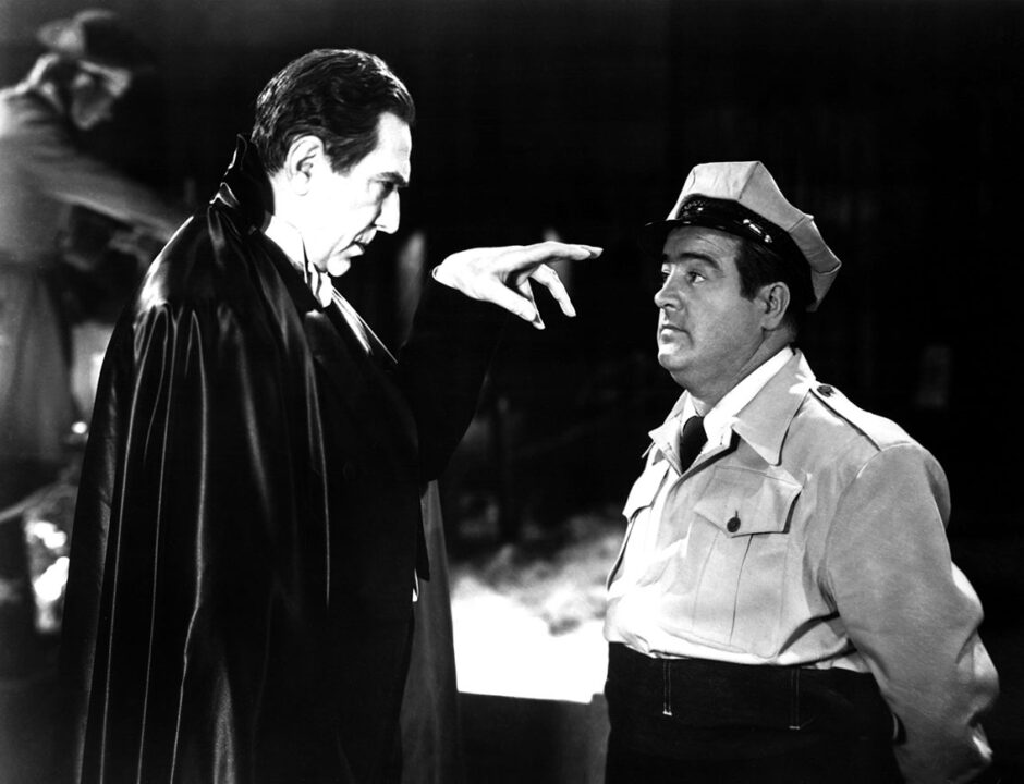 a black-and-white image from the 1948 horror comedy "Abbott and Costello Meet Frankenstein." On the left of the image is Bela Lugosi as Count Dracula, dressed in his black cape. He is gazing to the right of the photo with an intense gaze and has his left hand raised in a grasping/pointing manner as he attempts to hypnotize Wilber Grey (Lou Costello's character) on the right. Wilbur's eyes look to be getting glazed over as he falls under Dracula's spell.