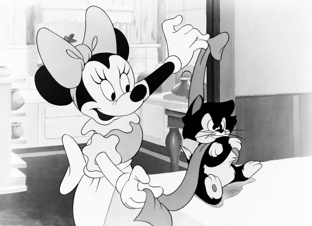 A still from the 1946 Disney animated short "Bath Day," depicting Minnie Mouse (standing on the left) smiling and toweling off Figaro the Cat (sitting on the right) following his bath. Figaro looks grumpy, and is frowning and folding his arms angrily.