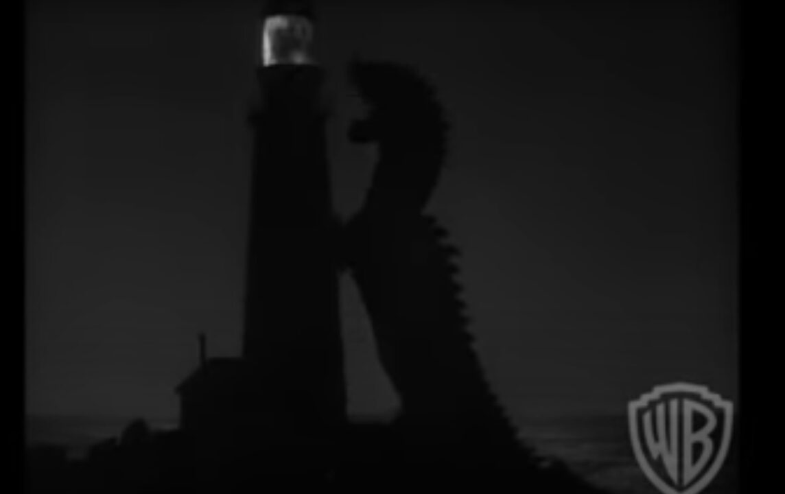 black-and-white image from the 1953 monster movie "The Beast From 20,000 Fathoms." It is a nighttime shot featuring a silhouette of the "rhedosaurus" rising out of the sea and extended up to attack a lighthouse, also in silhouette. The lighthouse's light provides the only illumination in the photo.