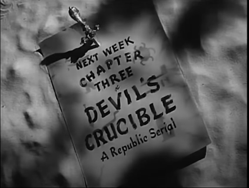 black-and-white still from the 1942 movie serial "Perils of Nyoka." It is the ending title card for Chapter Two, teasing the next chapter. The text is written in black lettering on an ancient looking parchment pinned into the desert sands by a knife. The stacked text reads: "Next Week, Chapter Three, Devil's Crucible, A Republic Serial"