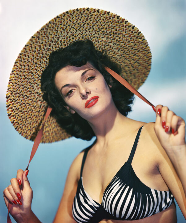 Actress Jane Russell (b. 1921) wearing a black and white bikini top while holding the red draw strings of a wide brim straw hat. Color publicity handout, slide. BPA#2 5854 