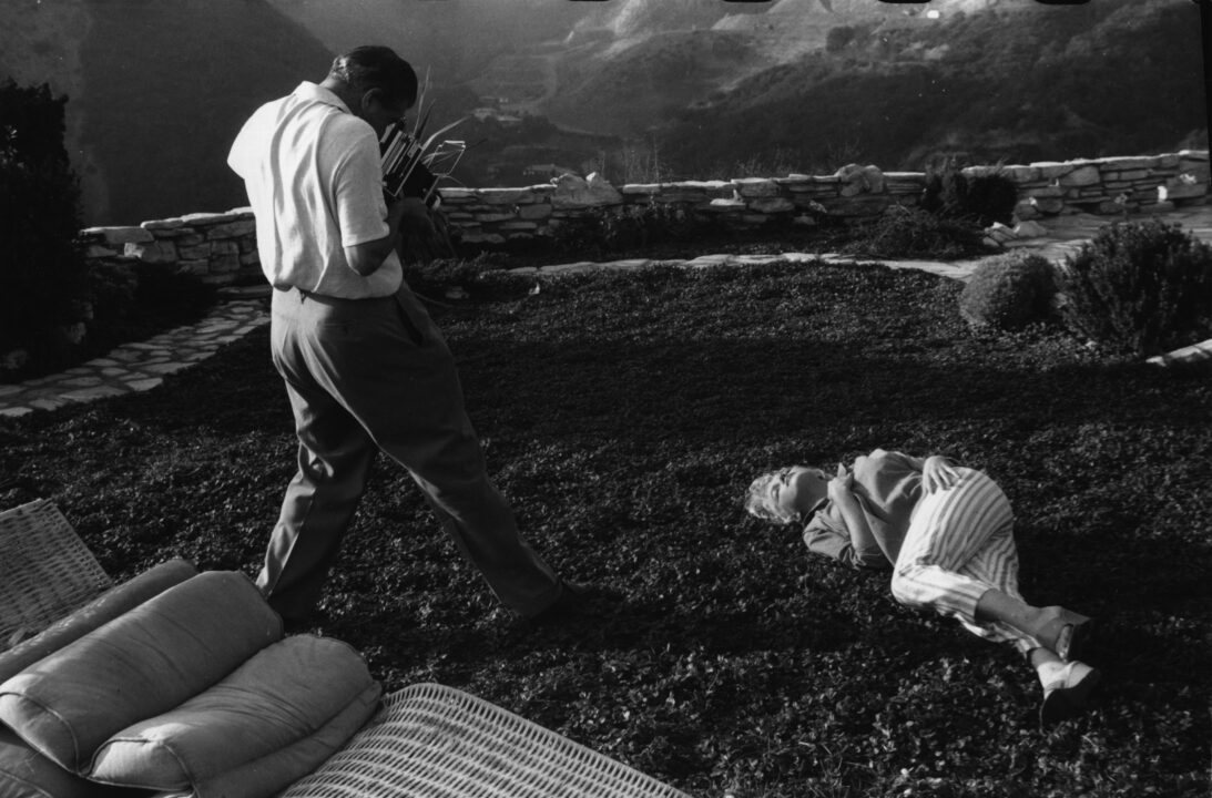1954: Wearing striped capri pants, Marilyn Monroe (Norma Jean Mortenson or Norma Jean Baker, 1926 - 1962) is photographed by Baron in the garden of her home. In the background is a view of mountainous countryside. 