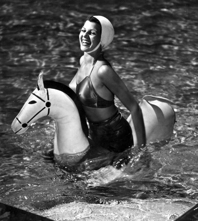 1940: Actress Rita Hayworth (1918-1987) swims with an inflatable horse on a break between filming. 