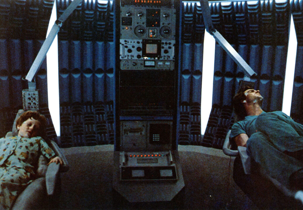 scene from the 1984 movie "Dreamscape." It is in a sleep lab, where the character played by Dennis Quaid, on the far right, is asleep in a chair with electrodes on his head, attached to a machine in the center. On the far left is a young boy set up in the same manner, as Quaid's character attempts to psychically enter the boy's dream to help him overcome a recurring nightmare.