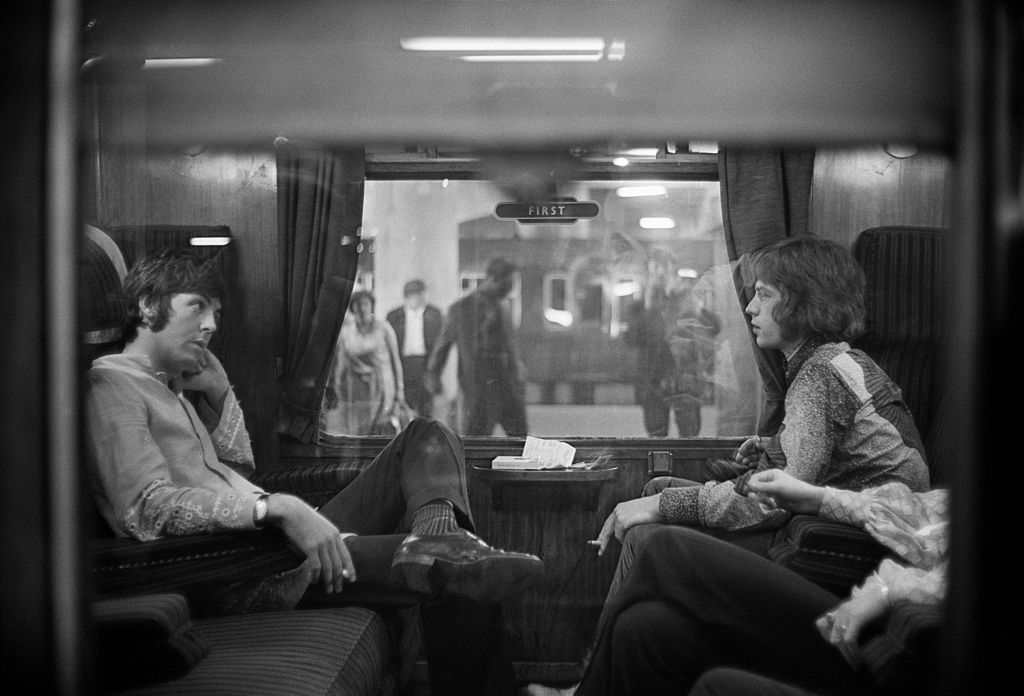 25th August 1967: Paul McCartney of the Beatles and Mick Jagger of the Rolling Stones sit opposite each other on a train at Euston Station, waiting for departure to Bangor