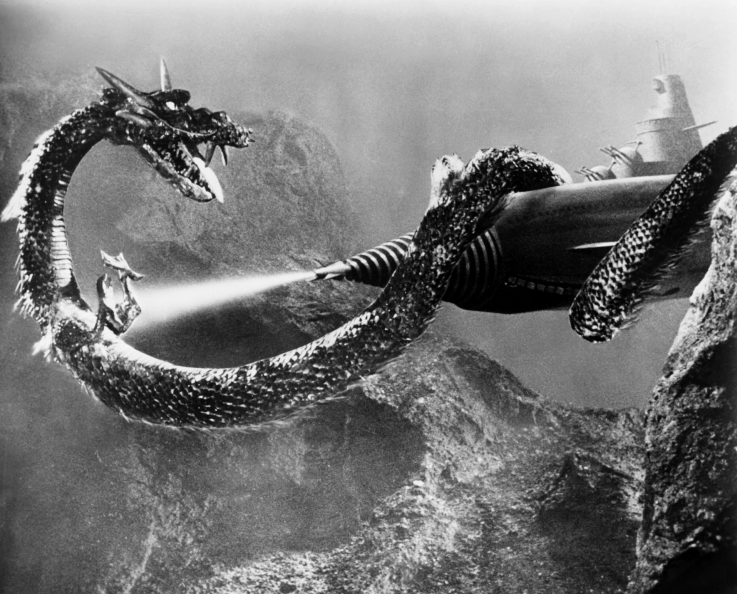 black and white image from the 1963 Toho movie "Atragon." It depicts the kaiju Manda, a large, serpent-like sea dragon, wrapped around a submarine.