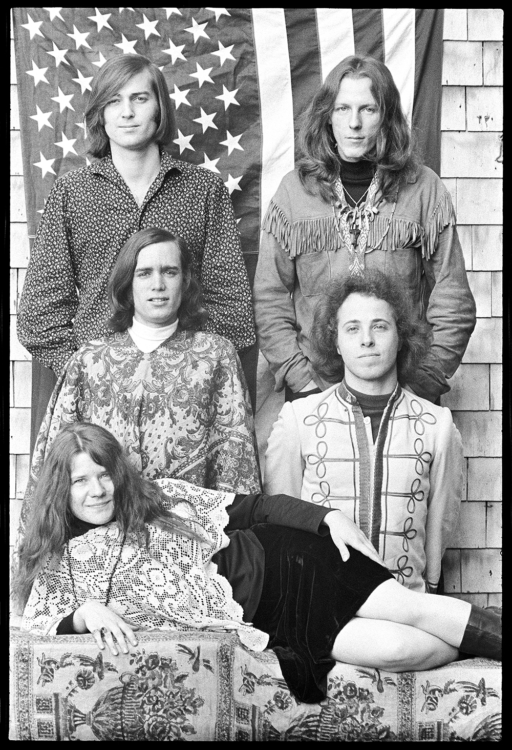 a black-and-white 1967 group photo of the band Big Brother and the Holding Company, with lead singer Janis Joplin lying on her side in front of the four other band members.