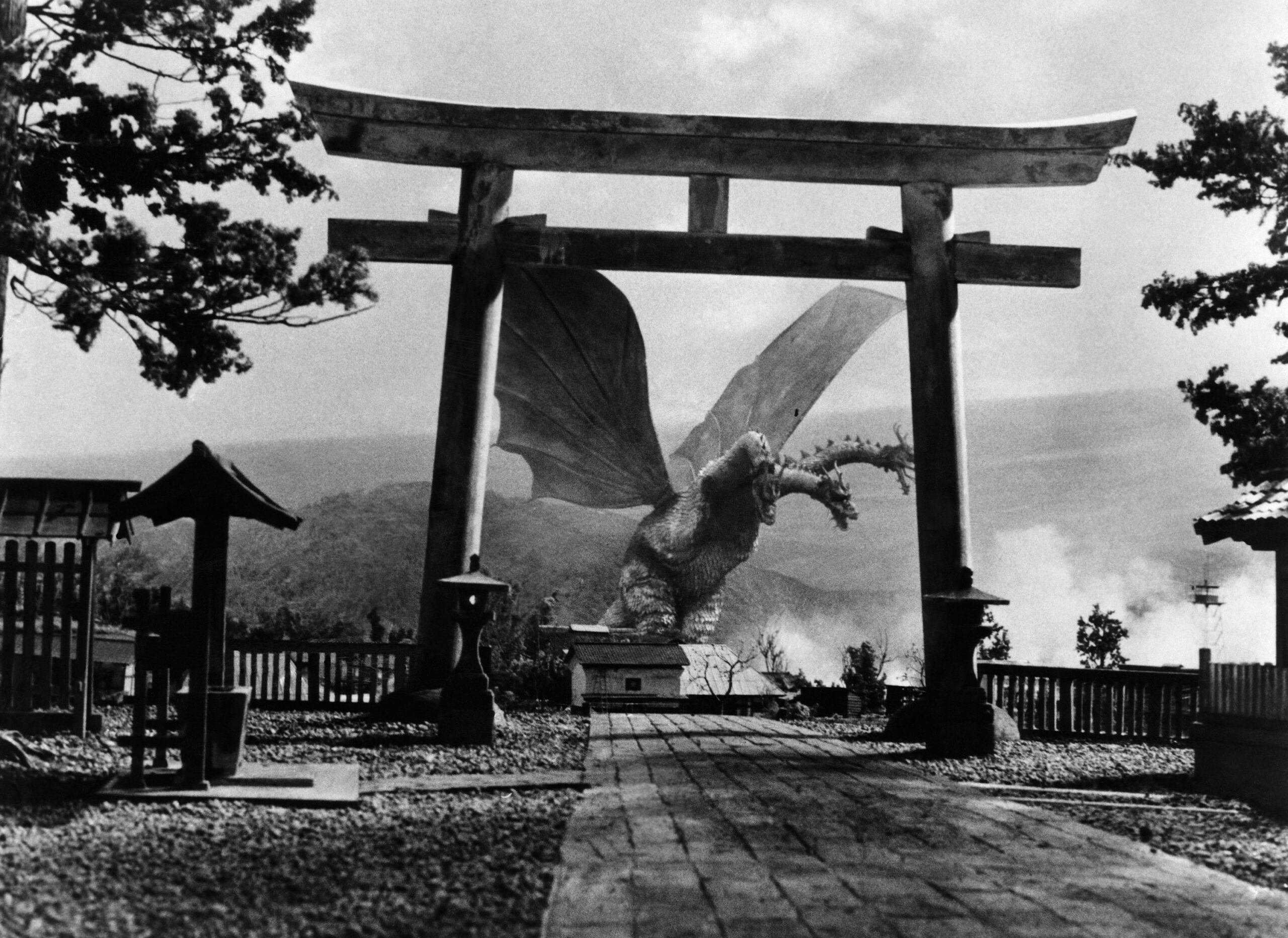 black and white photo from the 1964 Toho movie "Ghidorah the Three-Headed Monster." It depicts the titular kaiju, a large, dragon-like creature with three snake-like heads and large wings, about to attack a Japanese village.