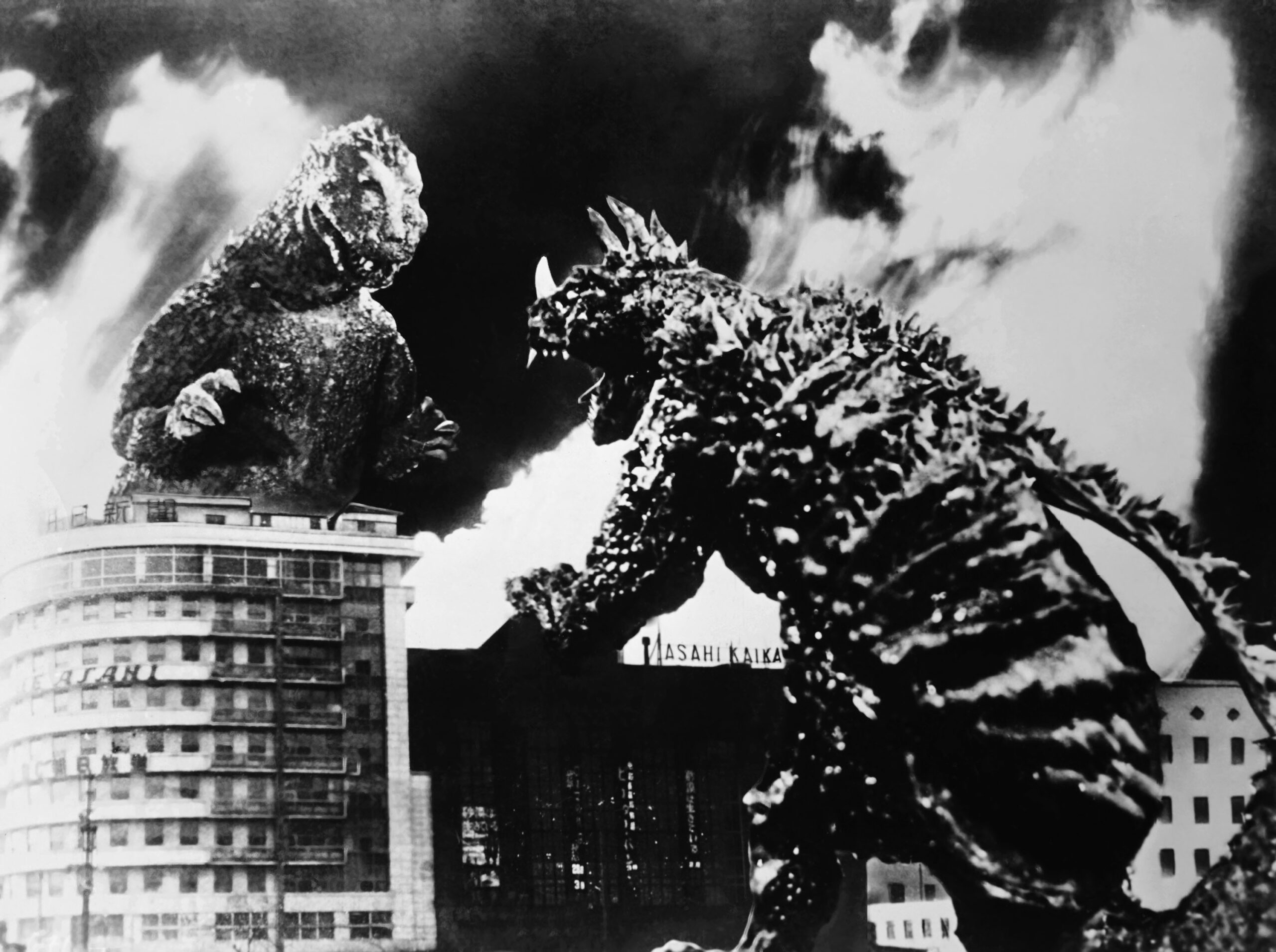 black and white shot from the 1955 Toho film "Godzilla Raids Again." It depicts Godzilla fighting with the four-legged, armored kaiju Anguirus. They are battling in a city that is engulfed in flames.