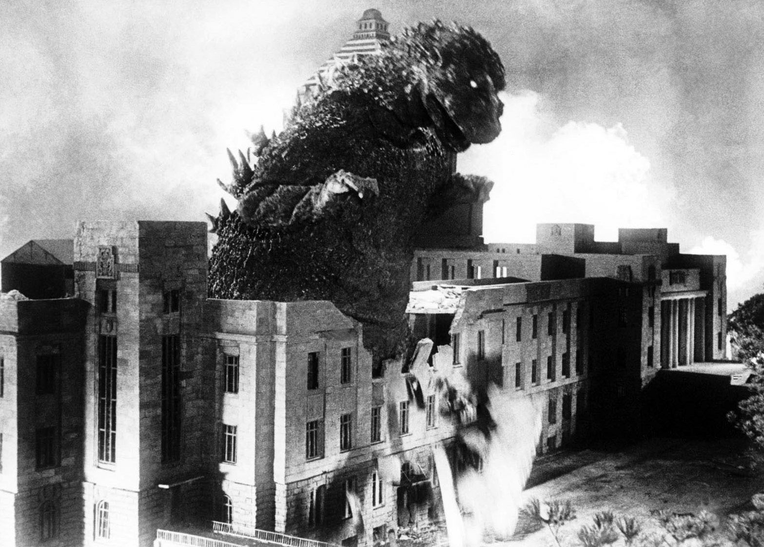 black and white photo from "Gojira (Godzilla)" (1954). It depicts Godzilla walking right through a building amid his rampage of destruction