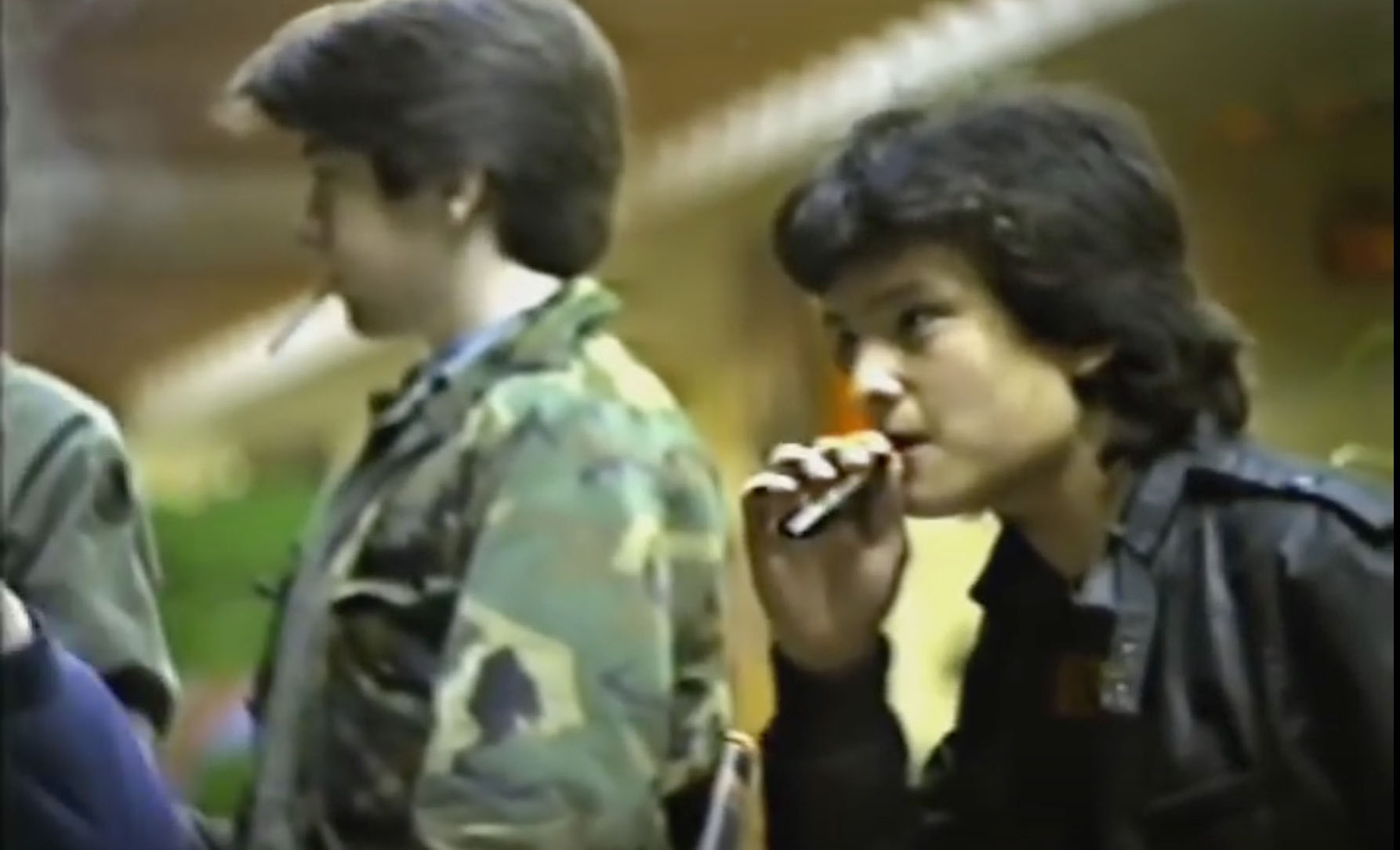 screenshot from the 1983 video documentary "Mall City." Pictured are two teen boys sitting at a Long Island mall, each smoking cigarettes.