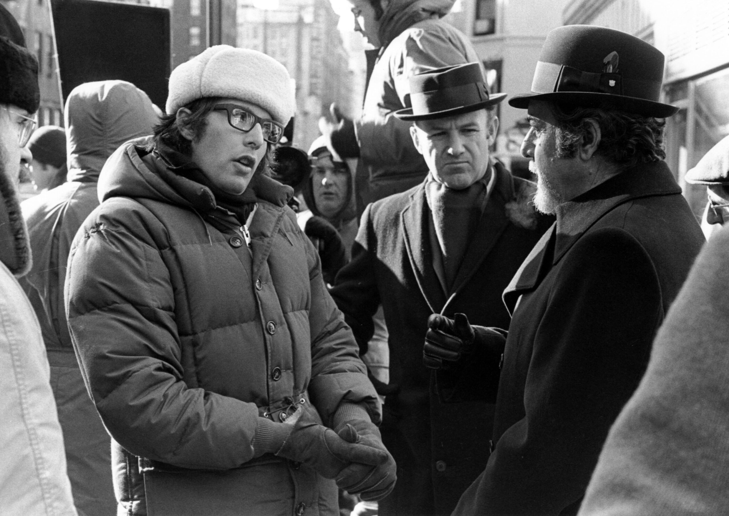 black-and-white BTS photo from the outdoor set of 1971's "The French Connection." Left to right: director William Friedkin, and stars Gene Hackman and Fernando Rey
