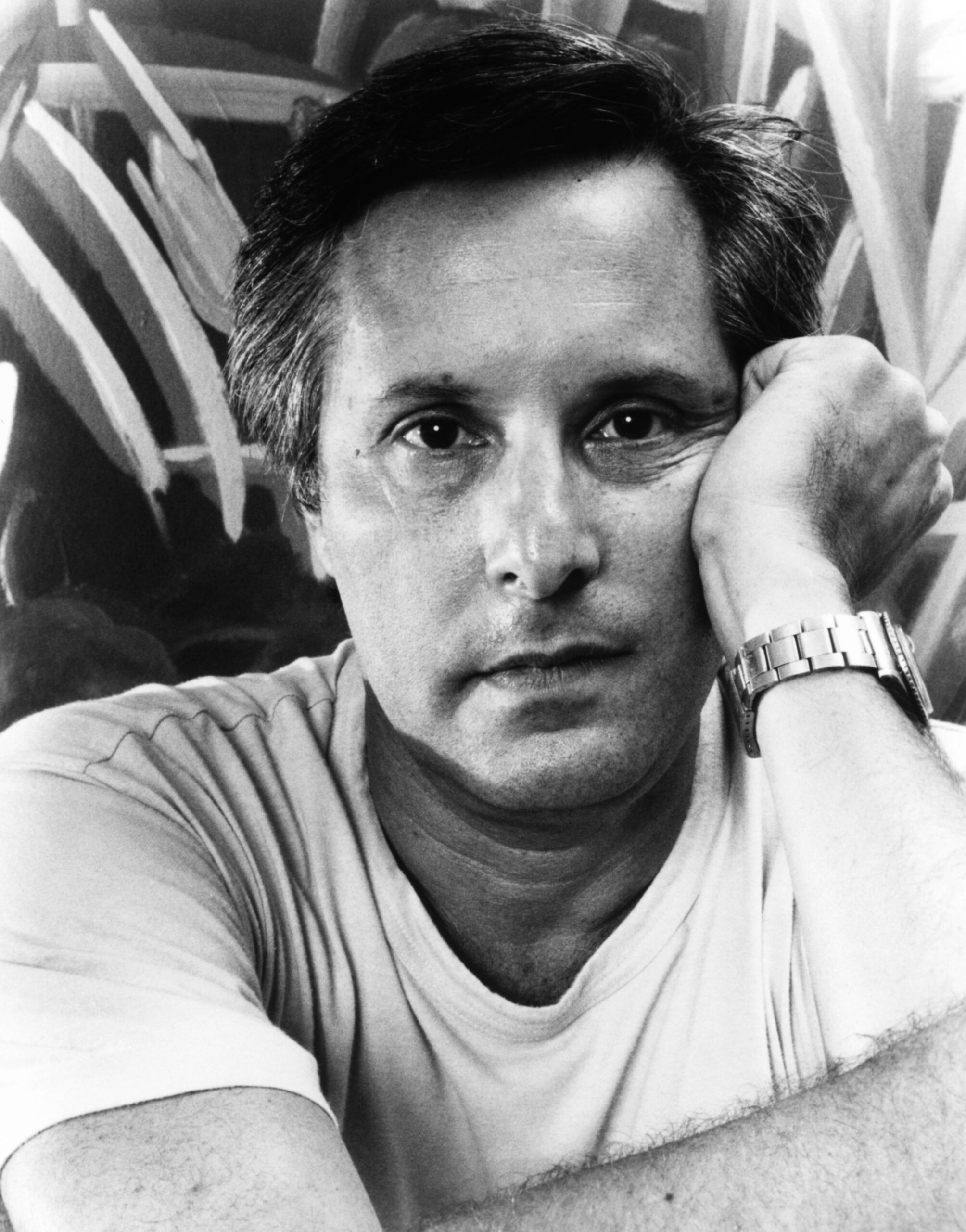 black-and-white close-up portrait photo of director William Friedkin on the set of the 1990 movie "The Guardian." He is resting his left cheek on his left hand, with his right hand supporting his bent left arm at the elbow.