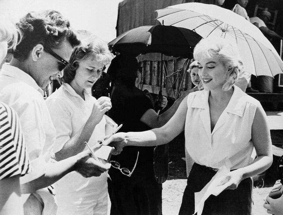 THE MISFITS, Marilyn Monroe (right) signing autographs on set, 1961