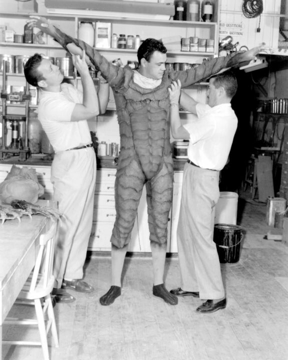 CREATURE FROM THE BLACK LAGOON, Jack Kevan, right, helps Ben Chapman, center, into his Creature costume, 1954