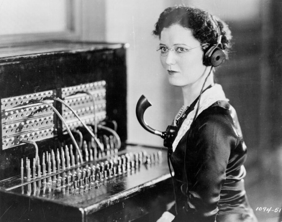 circa 1935: A telephone operator with headphones and a mouthpiece at a switchboard.