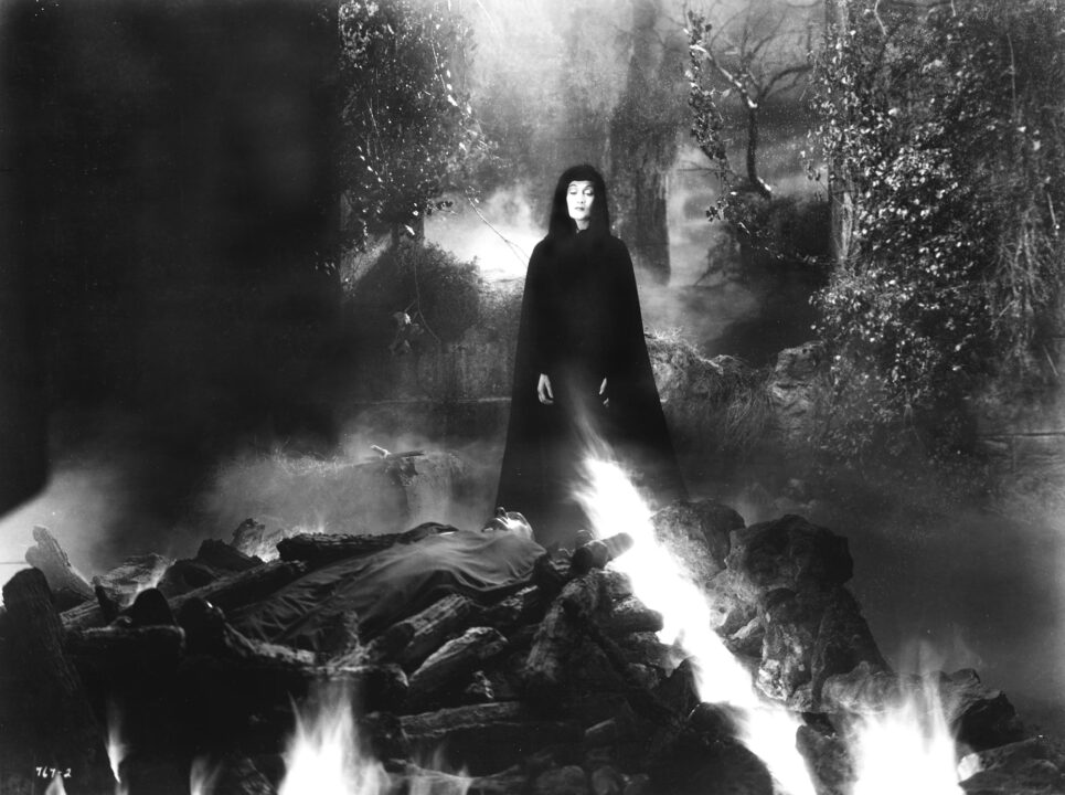 image from the 1936 film "Dracula's Daughter." The title character is seen wearing a black cloak and head covering at night, looking over a funeral pyre upon which is burning her father, Count Dracula.