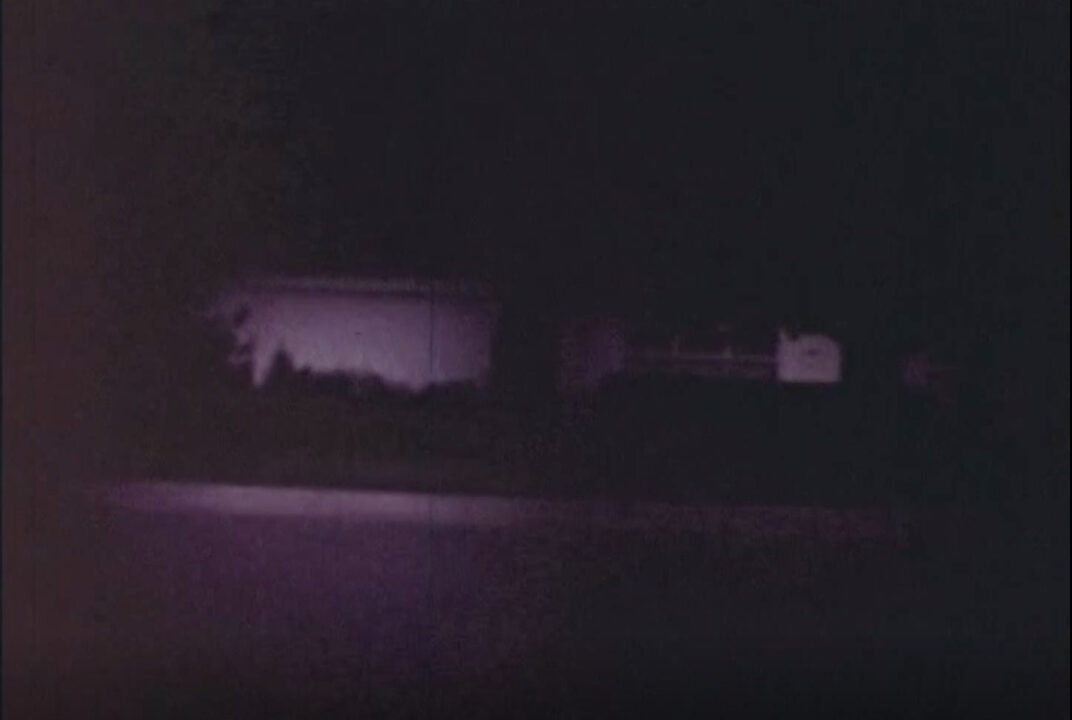 image from the 1977 short educational film "Halloween Safety." It is a view through as seen through the angle of a girl wearing a witch mask. We are seeing the nighttime neighborhood through just the eyeholes of the mask, with the vision very limited to demonstrate how unsafe the mask would be for trick-or-treating.