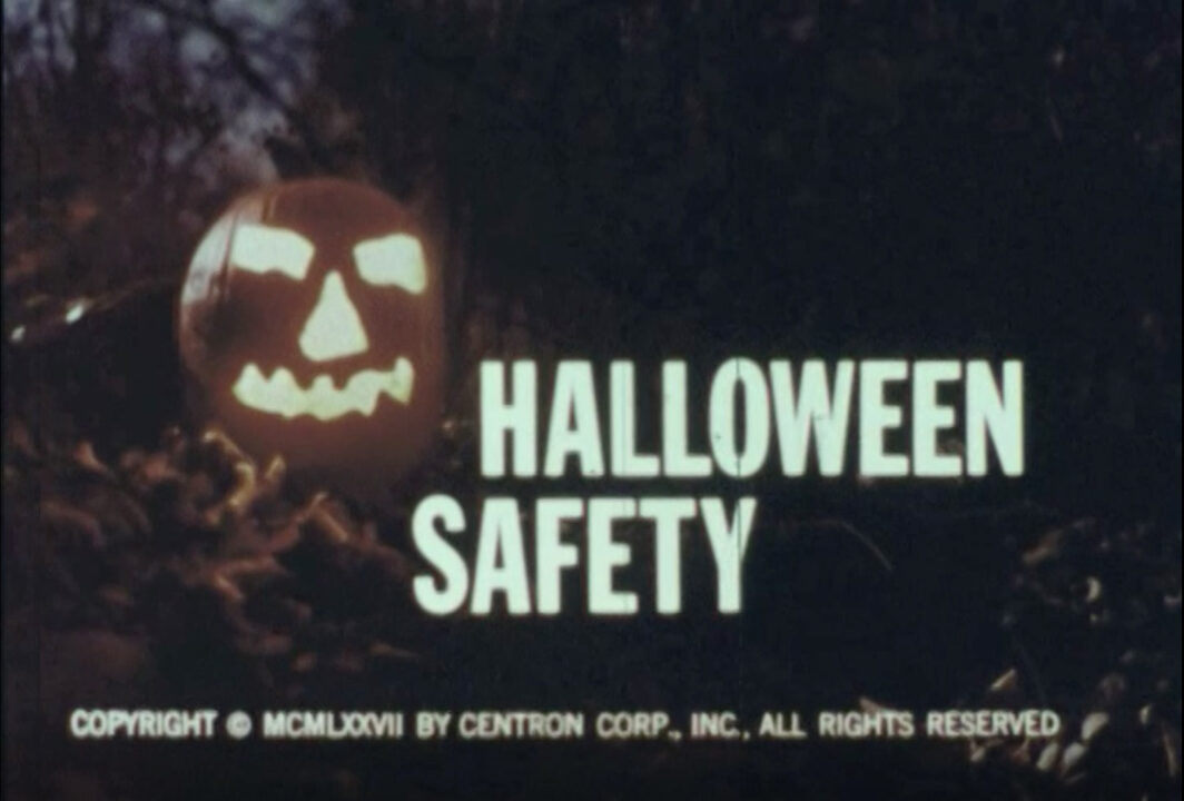title screen from the 1977 educational short film "Halloween Safety." To the left of the image is a lit jack-o-lantern, sitting among some leaves in a dark and spooky forest. Just to its right, in white lettering, is the film's title, "Halloween Safety."