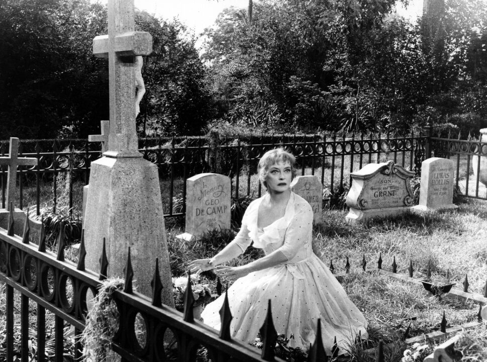 image from the 1964 movie "Hush... Hush Sweet Charlotte." It depicts star Bette Davis in a cemetery, crouched down in front of a tombstone but looking away at something seemingly in alarm.