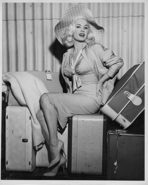 Actress Mamie Van Doren sitting in a glamorous pose on top of her luggage, as she arrives in New York with Trans World Airlines, Idlewild Airport, circa 1958. 