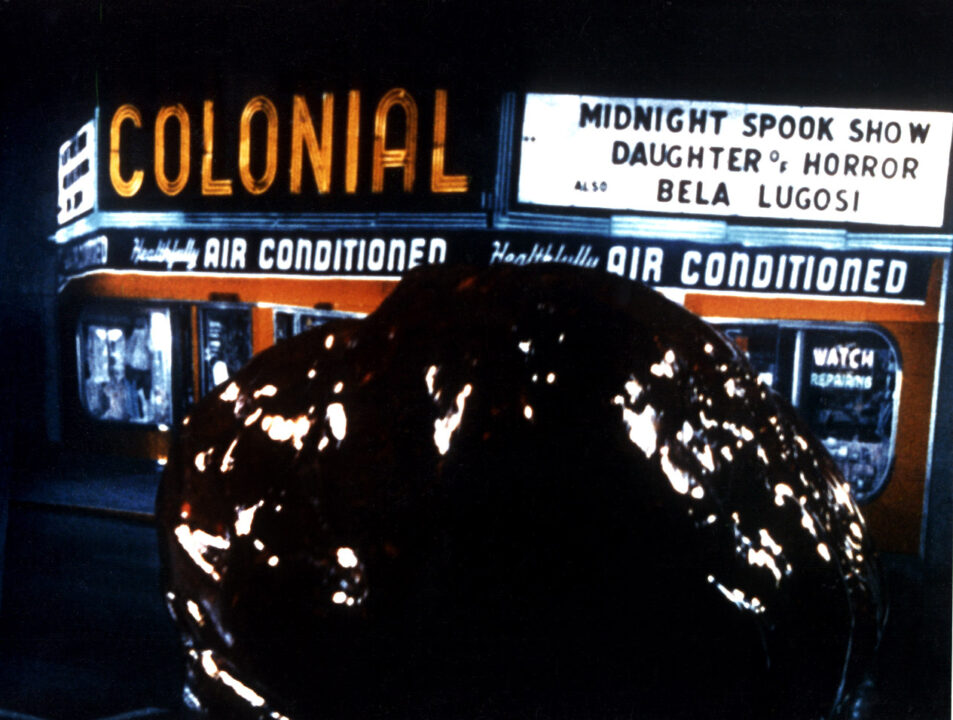 a scene from the 1958 movie "The Blob." the title creature, a giant, gelatinous, amoeba-like monster, is approaching the outside of a movie theater that is advertising a midnight "spook show."