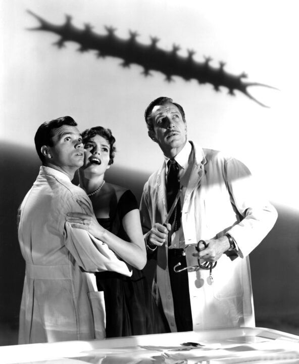 a black-and-white image from the 1959 horror movie "The Tingler." Pictured from left to right are stars Daryl Hickman, Patricia Cutts and Vincent Price. Hickman and Price are wearing white lab coats, and Cutts a dark-colored dress, and they are all looking up with concern at the shadow of a centipede-like "Tingler" on the wall above them.