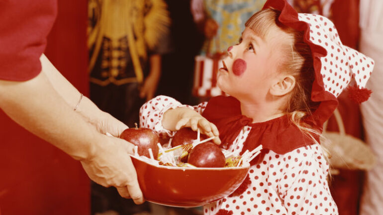 A little girl, wearing a clown costume for trick or treating, choosing a treat at Halloween, 1960s