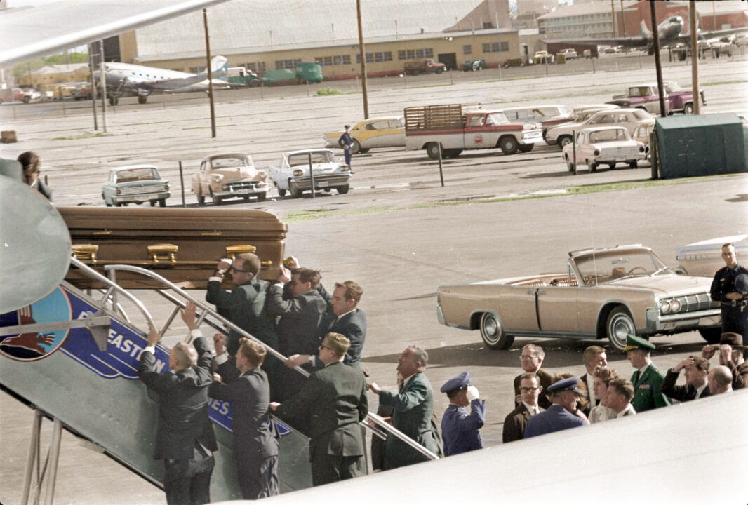 This colorized archival image shows President John F. Kennedy's casket as it is carried onto Air Force One at Love Field, Dallas, Nov. 22, 1963. Onlookers include Lawrence O'Brien, General Clifton, Jacqueline Kennedy, Kenneth O'Donnell, Dave Powers, and Evelyn Lincoln.