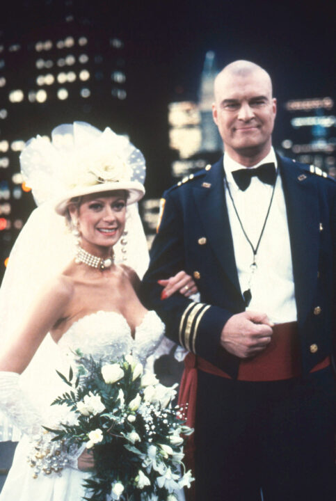 image from the 1991 <i>Night Court</i> episode "Get Me to the Roof on Time." Left to right are Cathy McAuley as Wanda Flinn, wearing a wedding dress and holding flowers, and Richard Moll as Bull Shannon, wearing a tuxedo as the two get married.