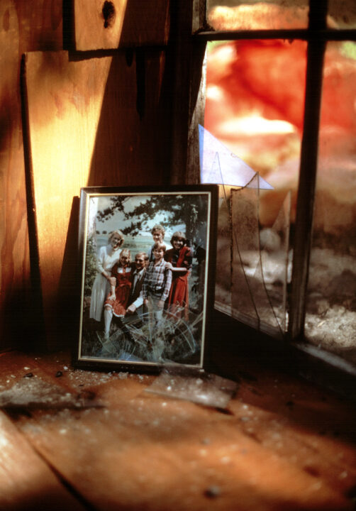 image from the 1983 TV movie 'The Day After.' It shows a family picture in a frame with shattered glass in front of a window. Outside, the sky is fiery orange and red, and in the background, part of a nuclear mushroom cloud can be seen.
