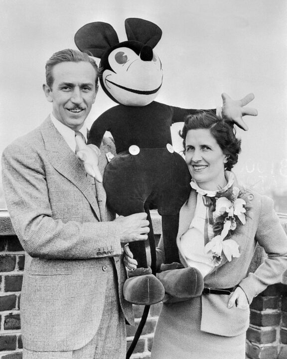 (Original Caption) Walt Disney, creator of the world-famous Mickey Mouse, is pictured with Mrs. Disney--who helped him invent his famous cartoon character--as they arrived at London, England recently, on a honeymoon that has been delayed for eight weeks. A stuffed Mickey Mouse is shown with the couple.