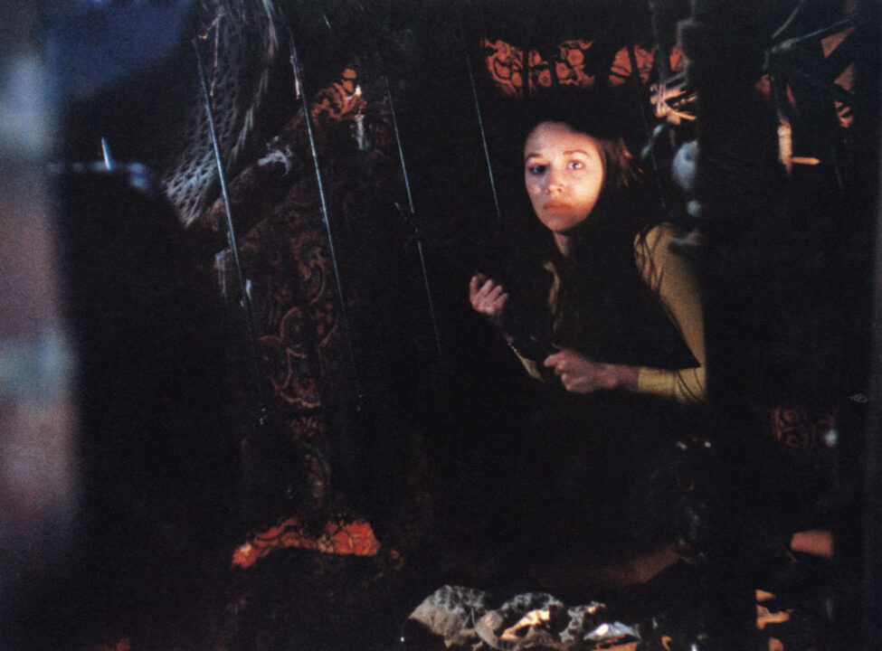 image from the 1974 slasher horror film "Black Christmas." It depicts star Olivia Hussey's character slowly entering a dark attic. She is holding a fireplace poker in a defensive way as she seeks the killer who has been terrorizing her sorority.