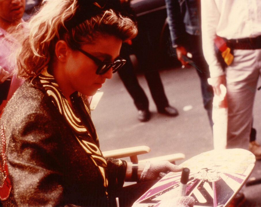 image from the 1985 movie "Desperately Seeking Susan" depicting star Madonna looking down at a skateboard while wearing sunglasses