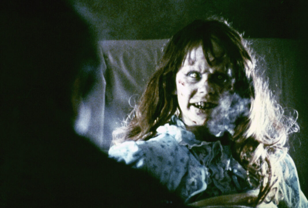 scene from the 1973 movie "The Exorcist." Linda Blair as Regan is seated up in her bed, her face made up into an evil "possessed" look. Her breath is visible in the coldness of the dark room.
