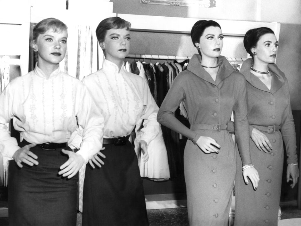 black and white photo from "The After Hours" episode of "The Twilight Zone" On the left is actress Anne Francis, wearing an early '60s style white blouse and black skirt. She is posing like a mannequin while standing next to a mannequin modeled after her and dressed as she is, to her left. To the left of that is a mannequin based on actress Elizabeth Allen, who is standing to the left of that mannequin. Allen is also posing mannequin-like, and is dressed in a darker women's business dress of the time.