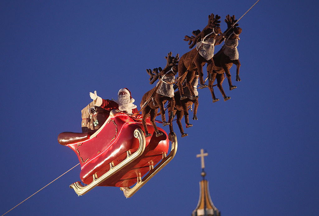 An actor dressed as Santa Claus waves from a suspended sleigh over a Christmas market as the Dom cathedral stands behind on November 25, 2013 in Berlin, Germany. Christmas markets, which traditionally sell mulled wine, stollen cake, Christmas tree ornaments and other crafts and are an essential part of German Christmas tradition, open across the country this week