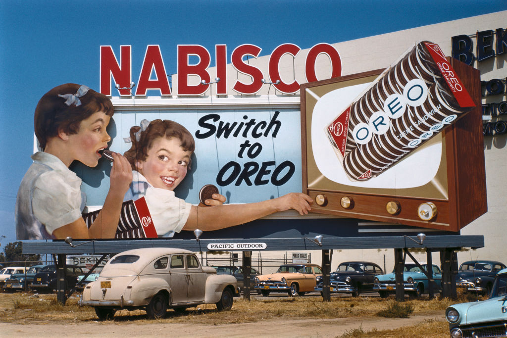 1950s: Nabisco Oreo billboard with two girls watching TV and old cars parked, old cars parked below, circa 1950 in Los Angeles, California. 1950s Nabisco Oreo billboard, girls, tv, old cars