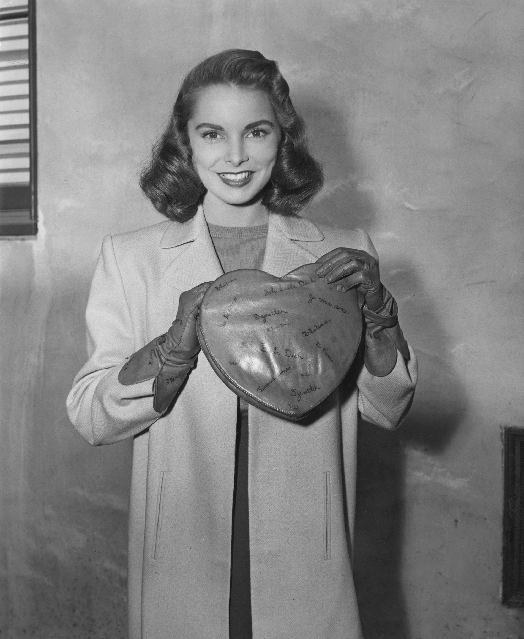 Janet Leigh models Valentine's Day accessories, a heart-shaped bag in red kidskin with the words 'I Love You' in various languages, and gloves to match, circa 1945.